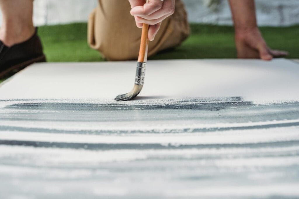 Personne peignant à la brosse sur une toile blanche.