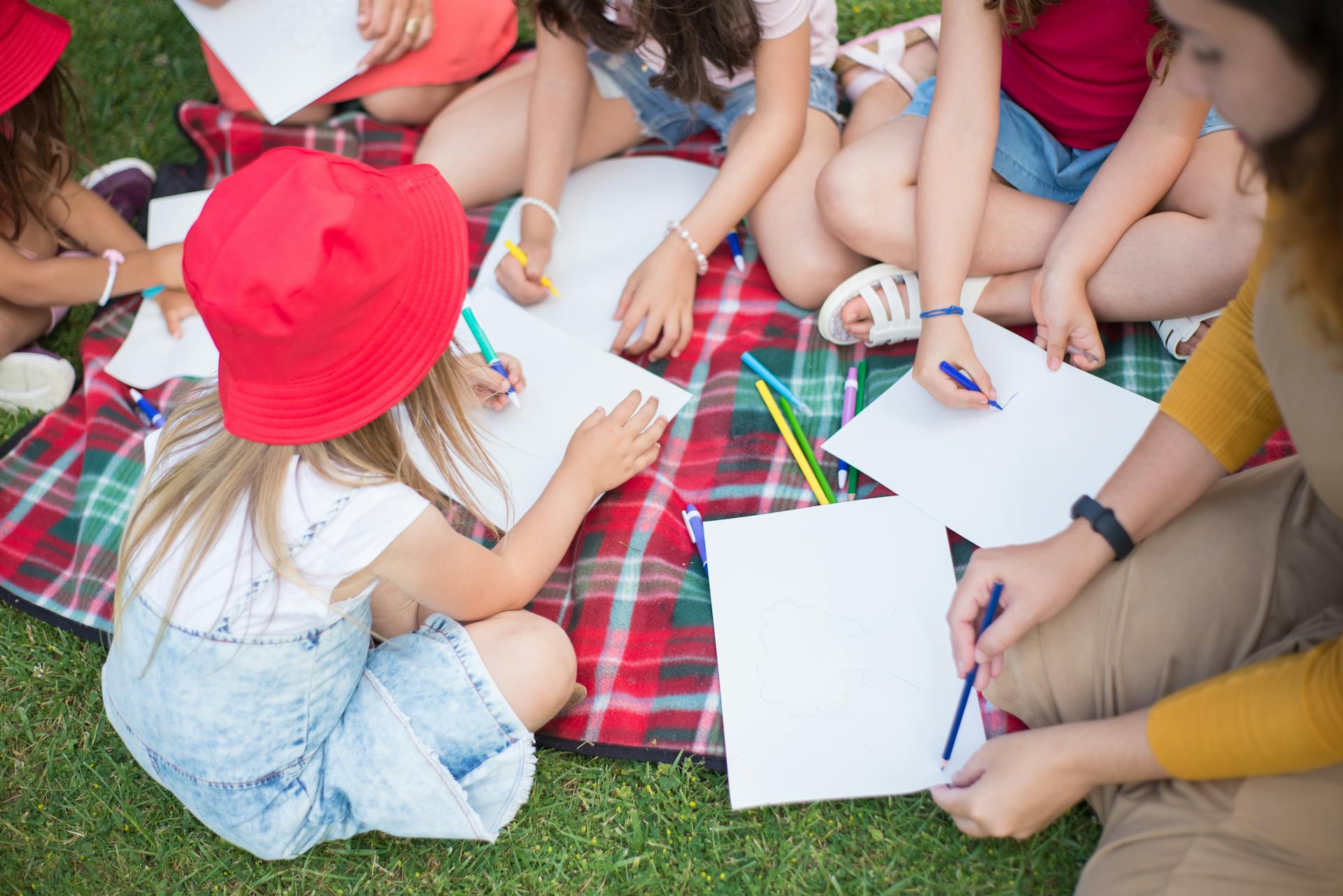 Enfants dessinant sur une couverture dans l'herbe.