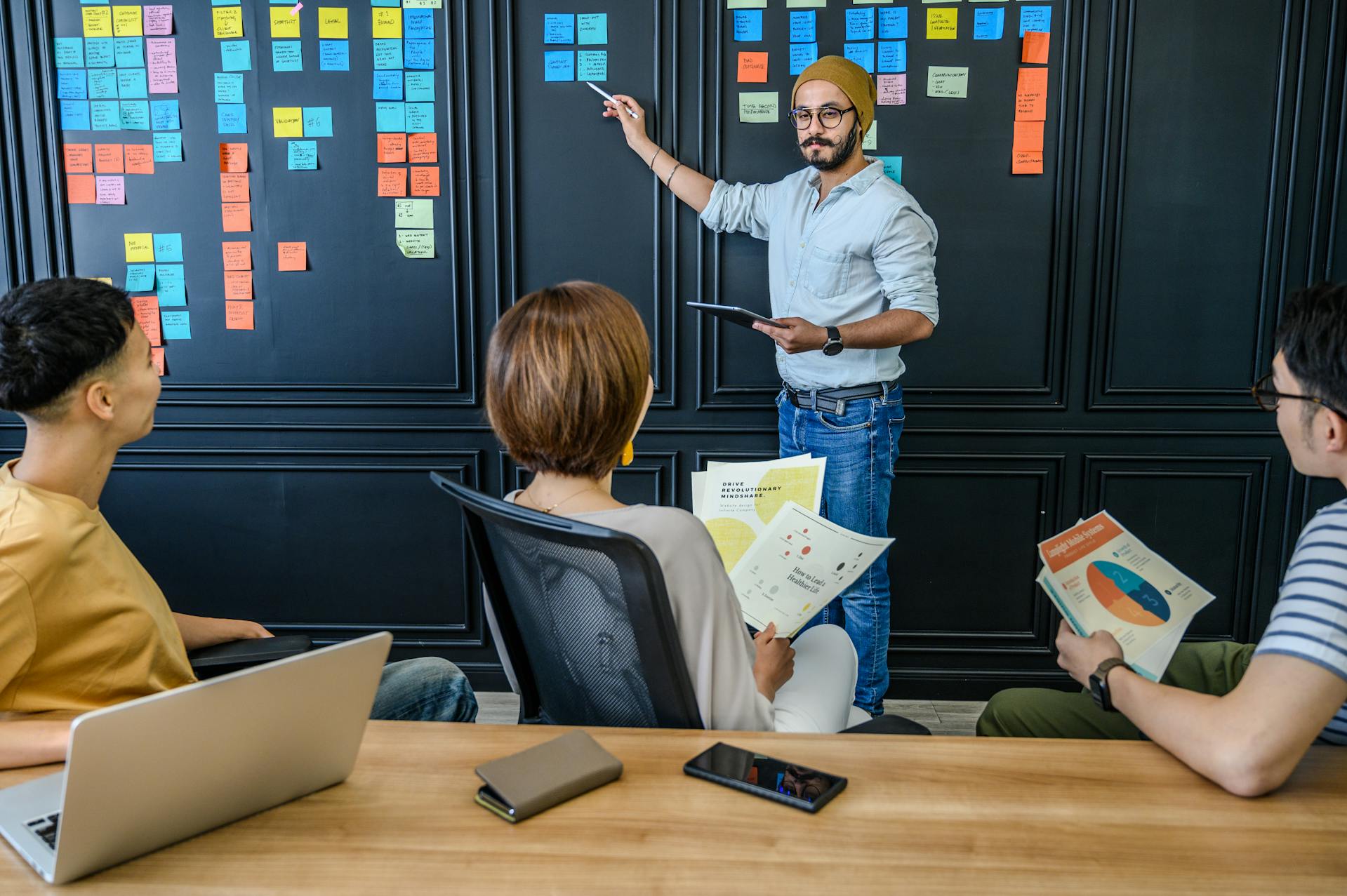 Réunion d'équipe devant un tableau de post-its colorés.