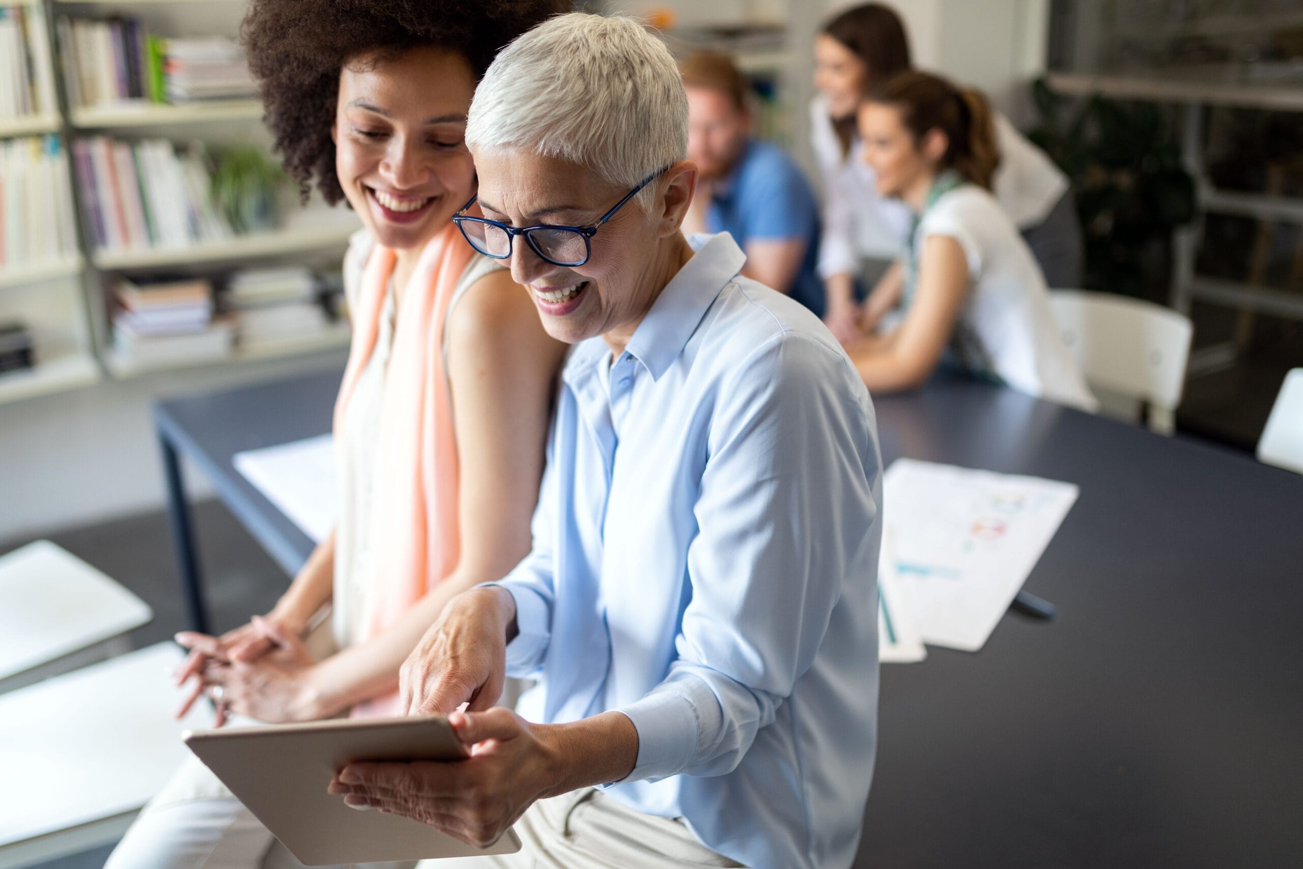 Personnes souriantes utilisant une tablette au bureau.