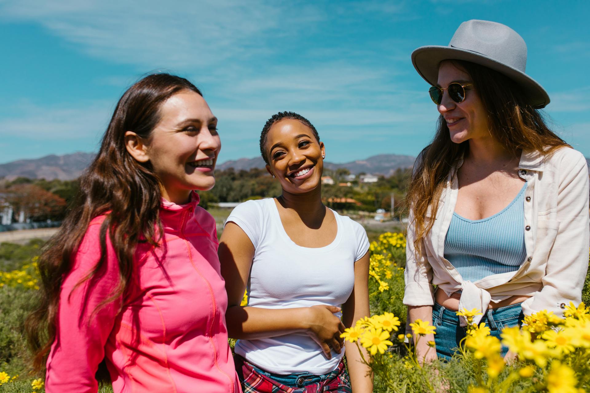 Trois femmes souriantes dans un champ de fleurs.